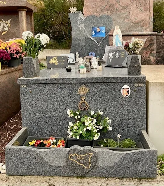 Tombe en granite gris ornée de fleurs, plaques commémoratives et motifs personnalisés.