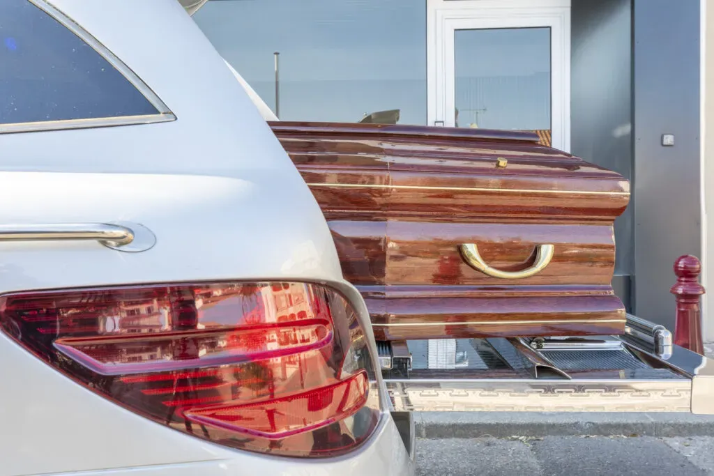 Cercueil en bois vernis posé sur le plateau coulissant d'un corbillard.