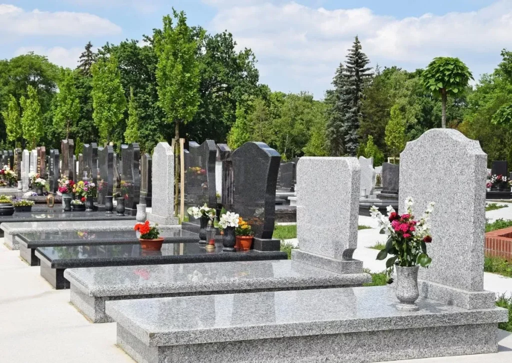 Alignement de monuments funéraires en granite gris dans un cimetière paysagé.